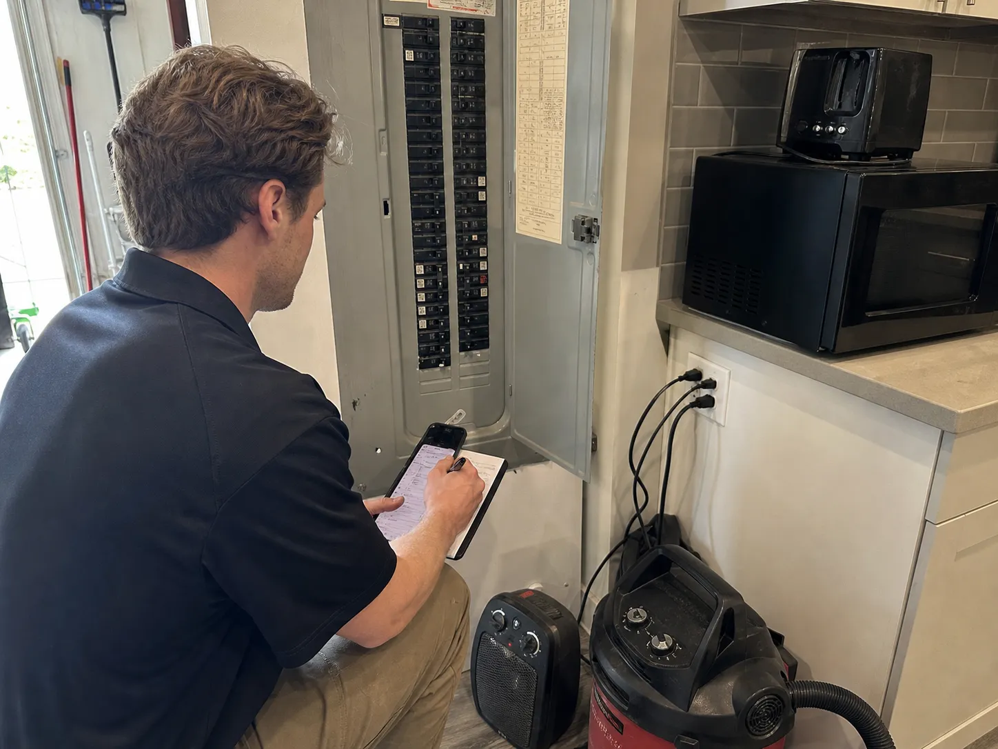 Coastal Comfort Electric technician documenting appliances and panel conditions while troubleshooting why a breaker keeps tripping.